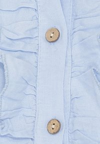 Lyseblåt stof med lodrette flæser og en rund træknapdetalje i midten. Blød tekstur og afslappet design.