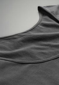 Nahaufnahme eines dunkelgrauen Stoff-Tanktops, das eine glatte Textur und eine geschwungene Ausschnittnaht auf einem neutralen Hintergrund zeigt.