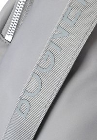 Bolso de tela gris con una superficie texturizada, cremallera plateada y una correa de logotipo en relieve prominente en un tono gris más claro.