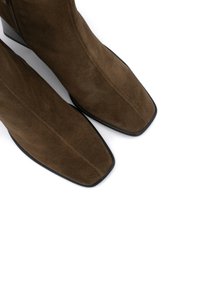 Botas de tobillo de ante marrón con puntera cuadrada y elegante tacón negro. La textura parece suave, con líneas limpias y detalles de diseño mínimos.