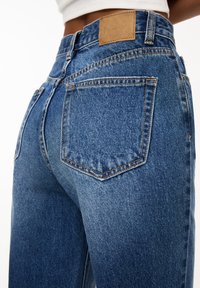 Blå denimjeans med hög midja, blekt utseende och kontrasterande sömmar. Inkluderar en märkesläderlapp vid den bakre midjan.