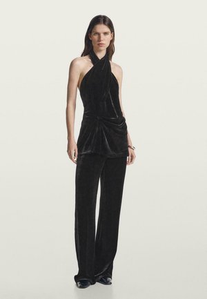 Top halter in velluto nero con parte anteriore drappeggiata e dettaglio di nodo, abbinato a pantaloni larghi coordinati, caratterizzati da una texture morbida e un'elegante silhouette.