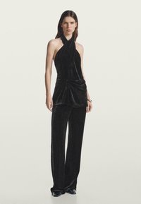 Black velvet halter top with draped front and knot detail, paired with matching wide-leg pants, featuring a soft texture and elegant silhouette.