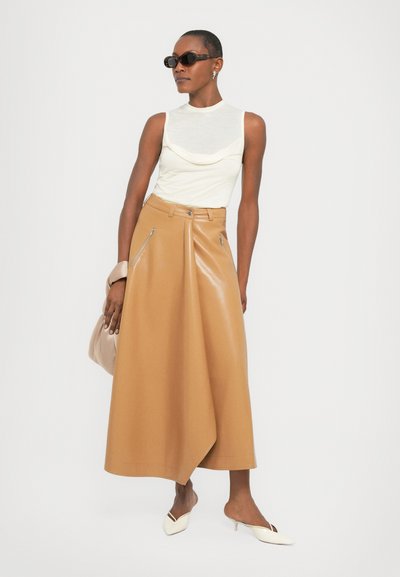 Beige, hoge taille leren rok met zijritsen, gecombineerd met een witte top met kraag en puntige witte hakken, accessorized met een zonnebril.
