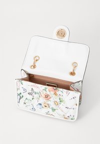 Sac à main blanc matelassé avec motif floral, garnitures en or, fermeture magnétique et intérieur beige. L'intérieur dispose d'une petite poche.