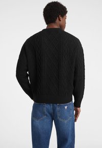 Maglione nero lavorato a maglia con un motivo a treccia strutturato e orlo a costine, abbinato a jeans in denim blu. Il maglione ha un collo rotondo.