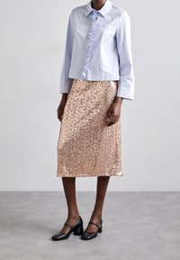 Ljusblå långärmad skjorta med rynkad placket, tillsammans med en knälång kjol i roséguld med paljetter och svarta klackskor med blockklack.