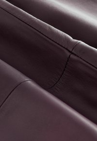 Textil de cuero burdeos oscuro con una textura suave, que presenta costuras prominentes y detalles de costura, dispuestos en capas superpuestas.