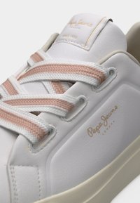 Baskets blanches Pepe Jeans avec lacets roses et blancs, semelle beige, et marquage sur le côté et la languette.
