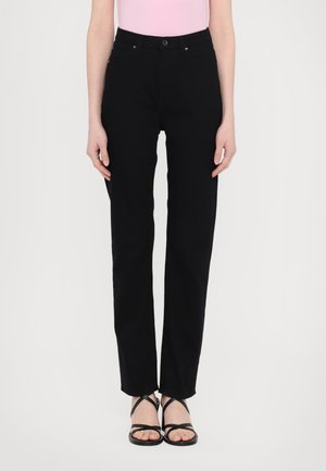 Black cotton straight-leg pants with a mid-rise waist, front pockets, belt loops, and a button closure; paired with black strappy sandals.
