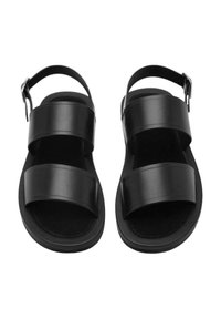 Sandalias de cuero negro con dos correas anchas, diseño minimalista, suela plana, correa ajustable en el tobillo con hebilla de metal y forro interior suave.