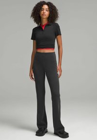 Mustapohjainen lyhyt paita punaisilla yksityiskohdilla, yhdistettynä tummanharmaisiin ribattuihin leveisiin housuihin ja tukeviin mustiin kengissä. Sileät, napakat kankaat.