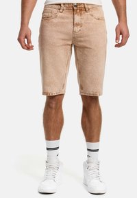 Short en denim beige avec une texture décolorée, cinq poches et des passants pour ceinture, assorti à des baskets blanches et des chaussettes rayées.