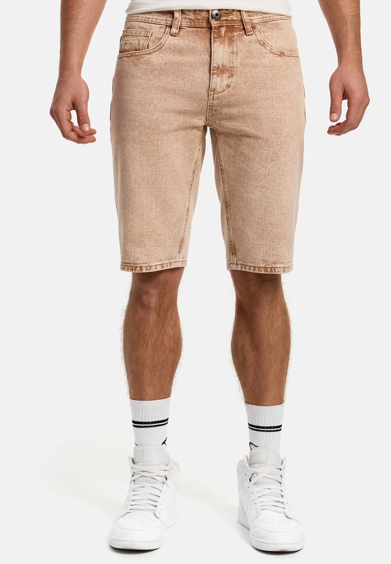 Short en denim beige avec une texture décolorée, cinq poches et des passants pour ceinture, assorti à des baskets blanches et des chaussettes rayées.