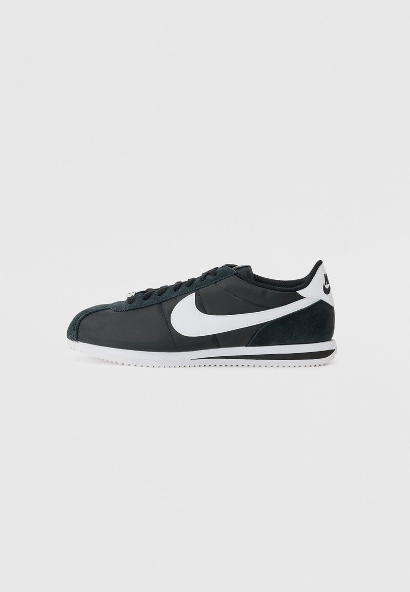 Fekete és sötétzöld Nike sportcipők, fehér Swoosh logóval, texturált velúr részletekkel, sima felső részel és fehér gumitalppal.