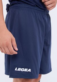 Shorts deportivos azul oscuro hechos de un tejido ligero con una cintura elástica y un logo blanco "LEGEA" en el lado inferior.