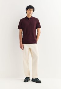 Bordó krátké rukávy polo tričko s límečkem, v kombinaci se světle béžovými kalhotami a tmavými botami. Jednoduchý design bez viditelných vzorů.