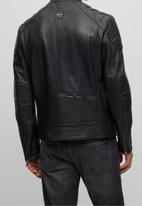 Svart läderjacka med texturerade paneler och sydda detaljer. Har en logotags på baksidan och dragkedjor vid ärmsluten. Bärs med mörka jeans.