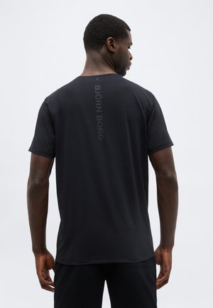 Muž otočený chrbtom, ktorý má na sebe čierne tričko s krátkym rukávom, na chrbte v strede potlačený vertikálny nápis "BJÖRN BORG".