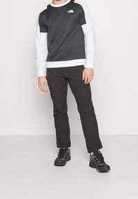 Maglietta a maniche lunghe nera e grigia con una texture a coste, maniche bianche e logo. Abbinata a pantaloni neri e scarpe scure.