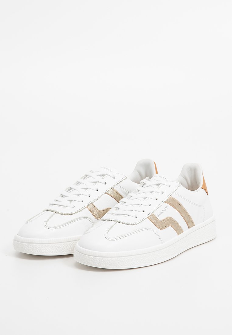 Białe sneakersy z beżowymi zamszowymi akcentami i brązową pętlą na pięcie. Posiadają teksturowaną gumową podeszwy i sznurowania. Prosty, klasyczny design.