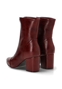 Botas de tobillo de cuero rojo con una textura suave, puntera redondeada y tacón cuadrado grueso. Presenta detalles de costura y un diseño ajustado en la parte superior.