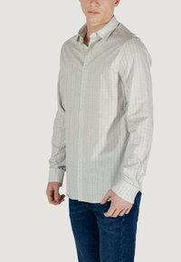 Camicia a maniche lunghe con bottoni di colore grigio chiaro, caratterizzata da un motivo geometrico sottile. Realizzata in tessuto morbido, presenta un colletto classico e polsini singoli.