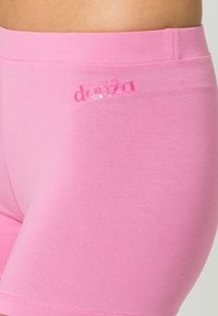 Różowe bawełniane szorty mają gładką fakturę, dopasowany krój oraz logo nadrukowane na pasie. Materiał wydaje się miękki i elastyczny.