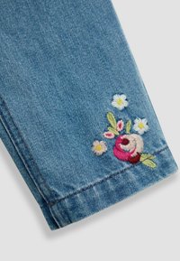 Denimstoff mit rosa und weißen Blumenstickereien am Saum, ausgestattet mit kleinen Blumen und detaillierten grünen Blättern.