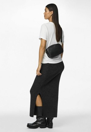 Bolso cruzado de piel negra llevado sobre una camisa blanca, combinado con una falda de punto gris oscuro con una abertura lateral y botas negras hasta la rodilla.
