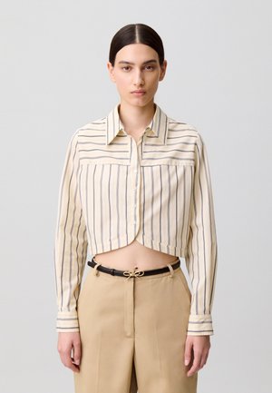 Camisa corta abotonada en beige claro con rayas verticales azul marino, con cuello abierto y mangas largas con puños abotonados.