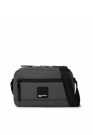 Bolso bandolera rectangular gris con bolsillo frontal con cremallera, correa negra ajustable y parche con el logo de Karl Lagerfeld Jeans en el centro frontal.