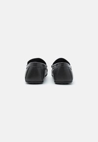 Schwarze Leder-Slipper, runde Form, strukturierte Oberfläche, Gummisohle mit kleinen Rillen, minimale Nähte an den Seiten.