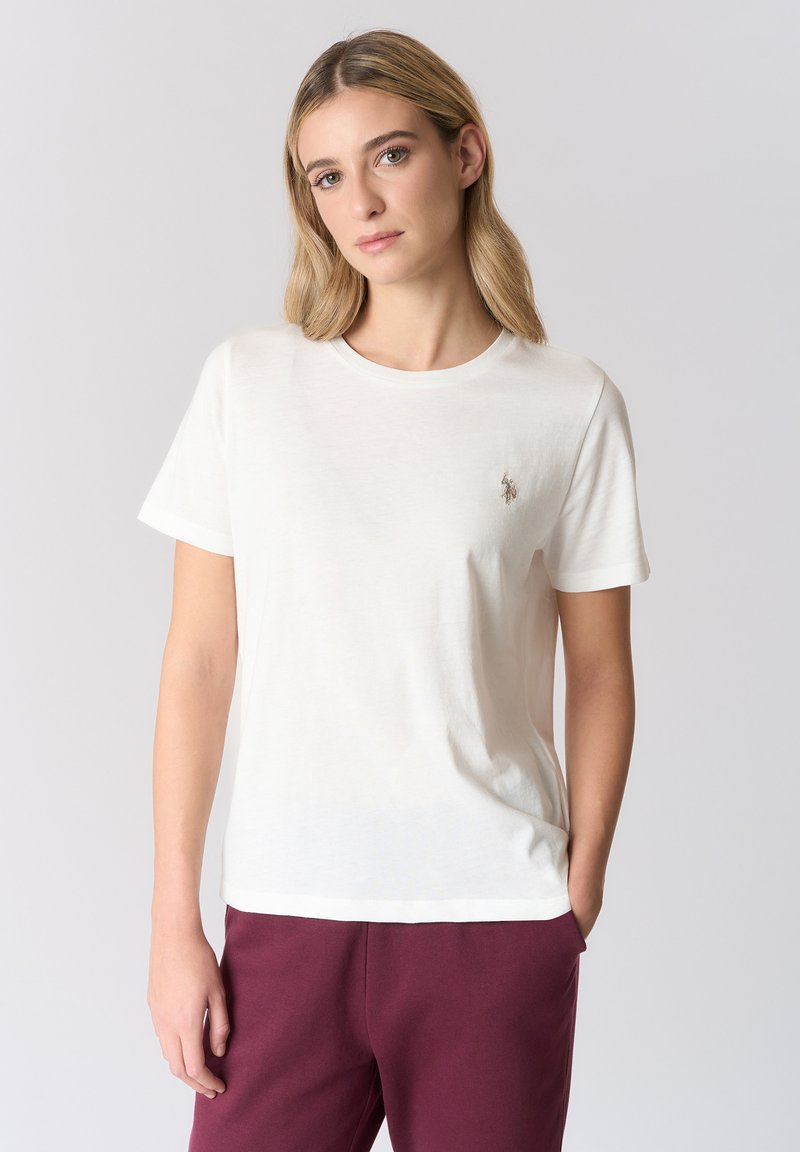 T-shirt in cotone a maniche corte color avorio con scollo rotondo e logo ricamato sul petto. Abbinata a pantaloni della tuta bordeaux.