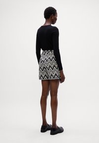 Maglietta nera a maniche lunghe, aderente in vita. Pantaloni corti con una fantasia a zigzag in bianco e nero. Scarpe nere con una finitura liscia.
