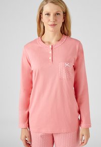Ensemble de vêtements de détente en coton dans un rose doux. Haut à manches longues avec patte de boutonnage, poche poitrine avec des pois blancs, pantalon assorti à pois.