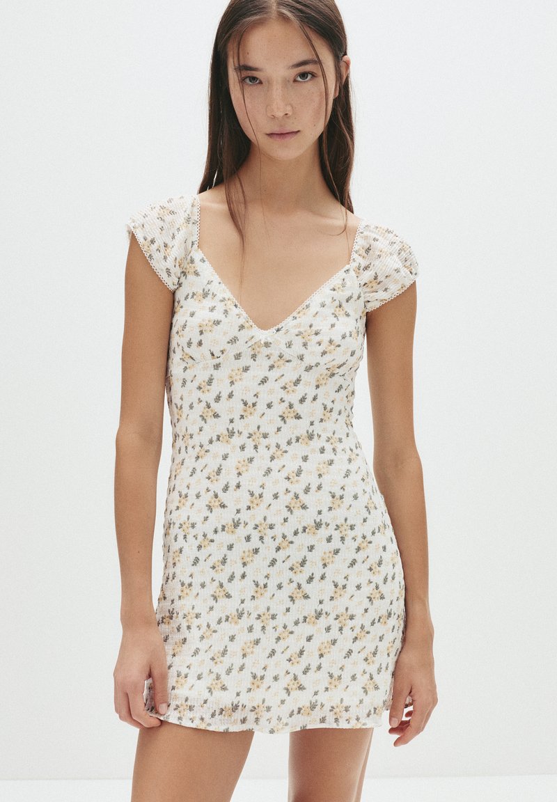 Weißes kurzes Kleid mit Blumenmuster, das über einen V-Ausschnitt und kurze Puffärmel verfügt, aus leichtem Stoff mit texturierter Oberfläche.