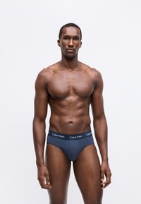 Tengerészkék pamut alsónadrág fekete derékpánttal, amelyen a "Calvin Klein" logó található. Testhez simuló fazon, sima textúra, és nincsenek látható minták.