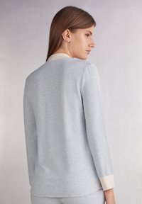 Helles blaues Langarm-Oberteil mit weicher Textur; verfügt über einen cremefarbenen Kragen und Manschetten. Einfaches, lässiges Design mit lockerer Passform.