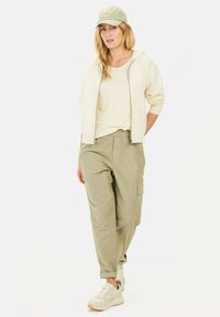 Letvægtscreme zip-up hættejakke, beige T-shirt, olivengrøn cargo-buks med lommer og beige sneakers, sat sammen med en lysegrøn kasket.