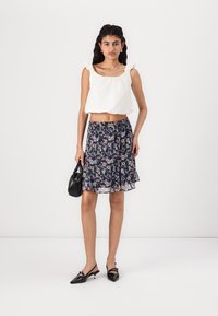Top blanc court avec des bretelles froncées, associé à une jupe florale marine et des accessoires noirs. Présente un design en couches et des chaussures noires à bout pointu.