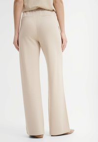 Beżowe spodnie z szerokimi nogawkami o gładkiej teksturze, z elastycznym pasem i dwiema tylnymi kieszeniami. Prosty design bez widocznych wzorów.