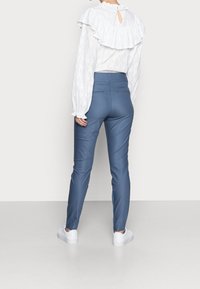 Pantalons ajustés bleu clair avec une texture lisse, associés à un chemisier blanc texturé avec un col froncé et des manches longues.