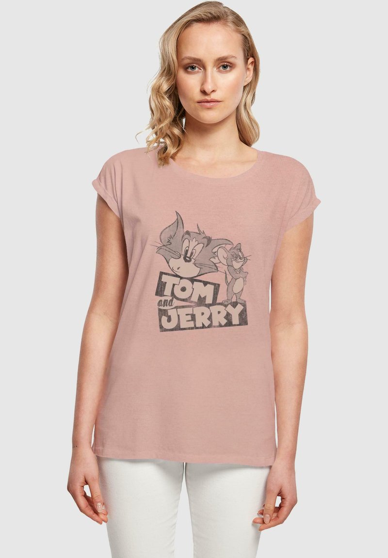 Svetlo roza majica s povzrnjenimi rokavi, ki prikazuje grafiko Toma in Jerija v odtenkih sive, z izrazitim besedilom "TOM IN JERRY" na dnu.