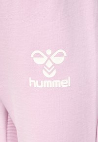 Ljusrosa sweatshirt-tyg med en vit logotyp med en abstrakt design och ordet "hummel" i små bokstäver. Slen textur.
