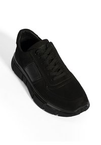 Schwarze Sneaker mit einem glatten, strukturierten Obermaterial, Schnürdesign und einer klobigen schwarzen Gummisohle. Verfügt über ein elegantes Panel an der Seite.