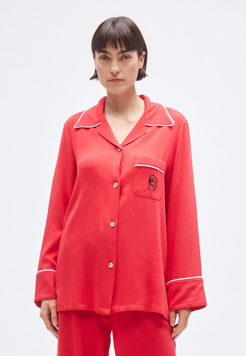 Červený saténový pyžamový top s bielou lemovkou, dlhými rukávmi, prednými gombíkmi a kapsou na hrudi s vyšívaným vzorom.