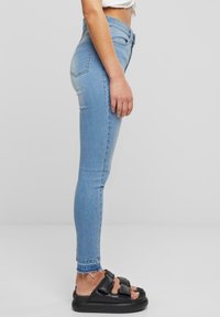 Fénykék skinny farmernadrág, középmagas derékkal és minimális kopással, fekete vaskos szandálokkal párosítva, dupla pánttal és vastag talppal.