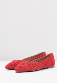 Červené ploché boty vyrobené z měkkého materiálu s perforovanými detaily na svrchní části, špičatou špičkou a plochou podrážkou pro pohodlí.