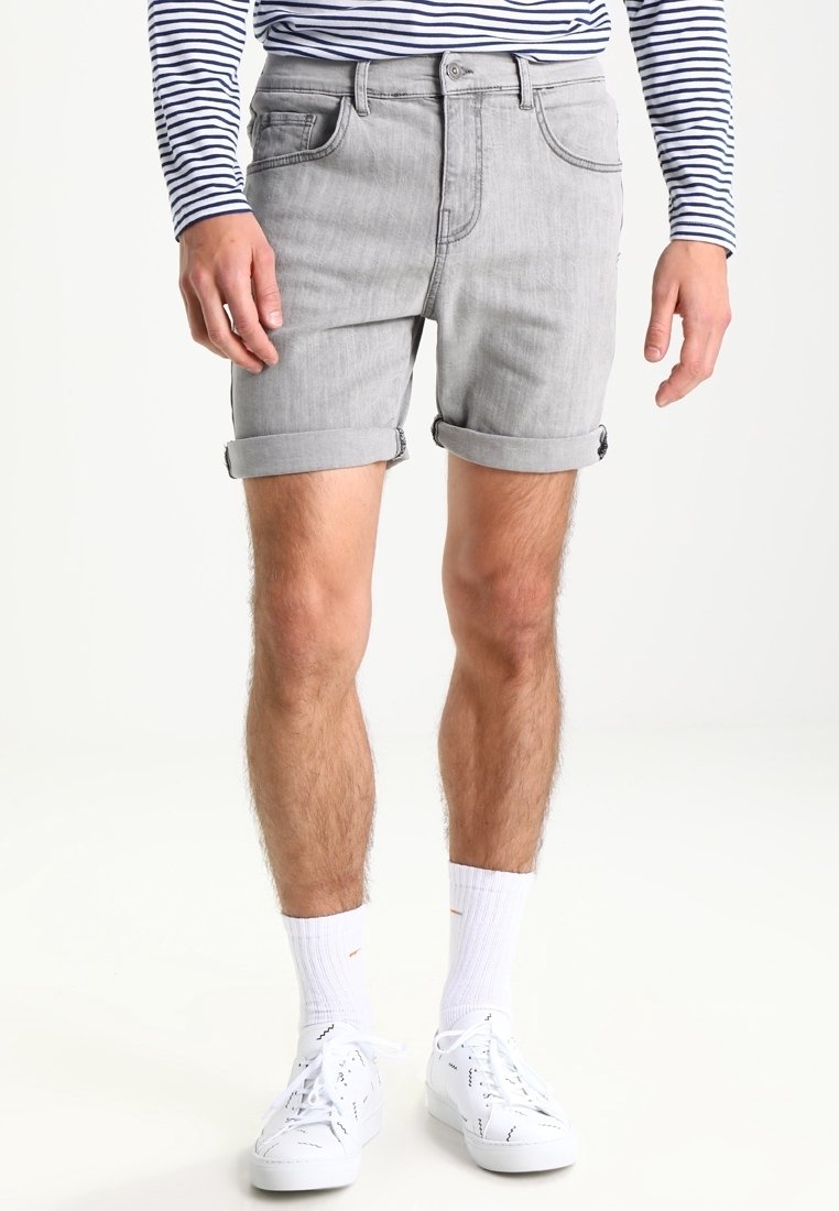 Homme portant un short en jean gris clair retroussé, des baskets blanches, des chaussettes blanches et une chemise à manches longues rayée bleu marine et blanc.